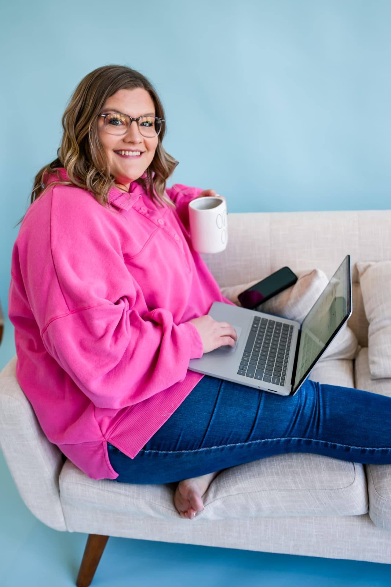 Shelb smiling on the couch with her laptop and a mug
